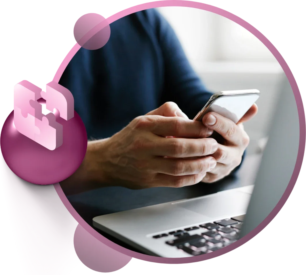 Person holding a smartphone with a laptop in the background