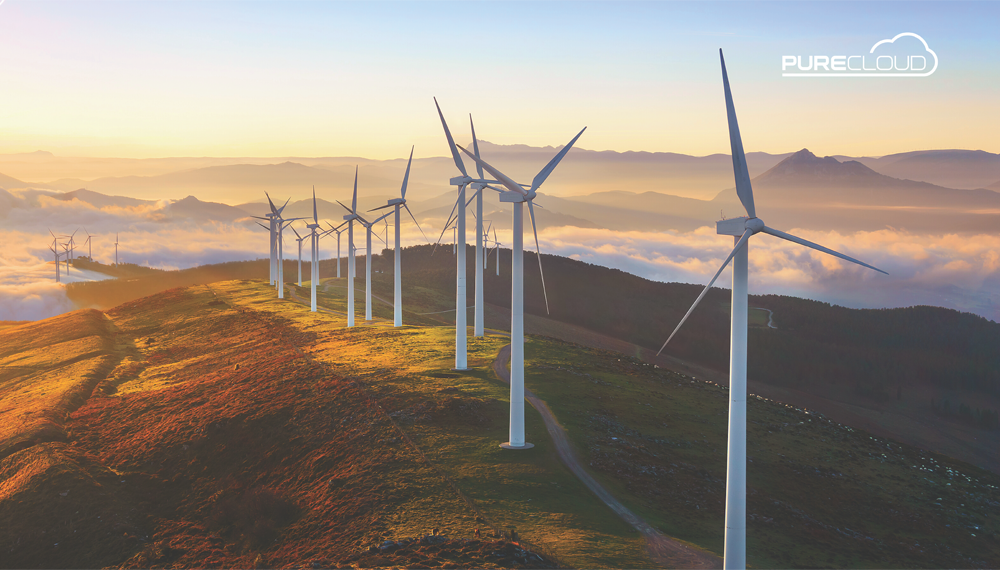 Wind turbines positioned on a hillside with a backdrop of mountains and clouds during sunrise, showcasing renewable energy technology.