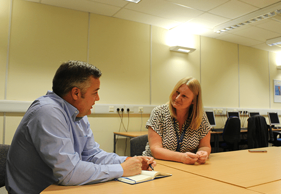 A man and woman talking, while sitting aound a table